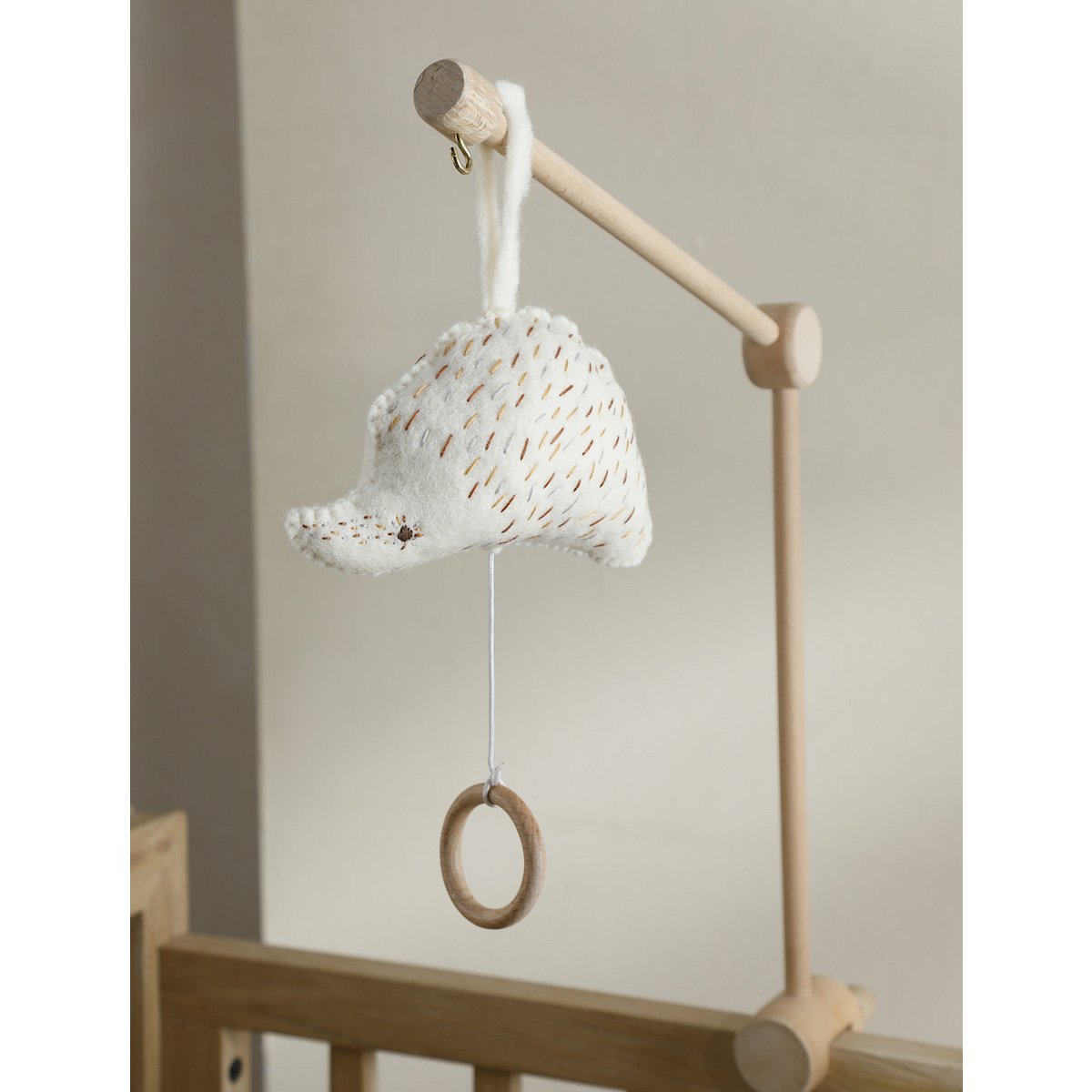 Baby mobile with textured ball and wooden ring hanging from a wooden stand against a neutral background