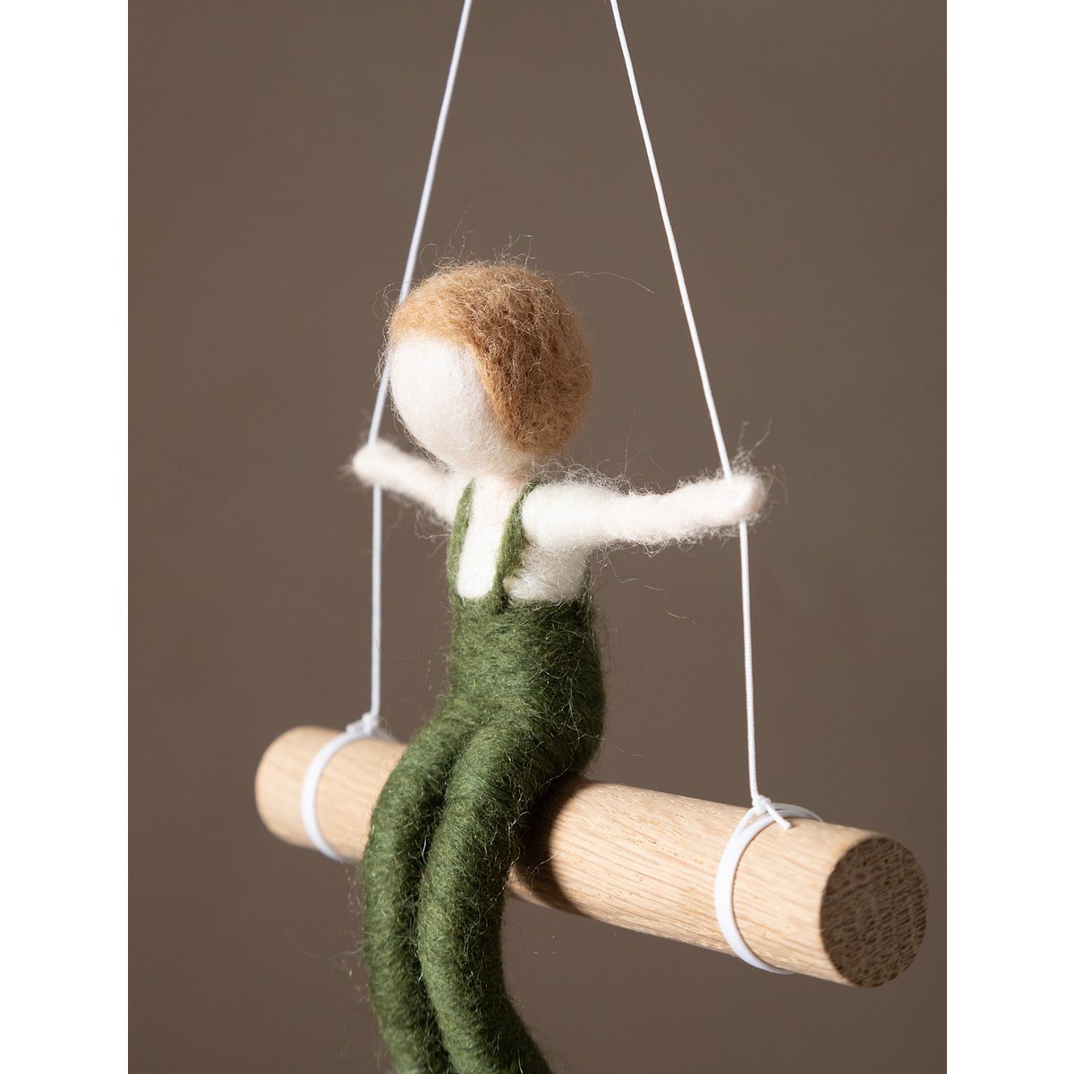 Textile figure of a person in green overalls on a swing against a brown background