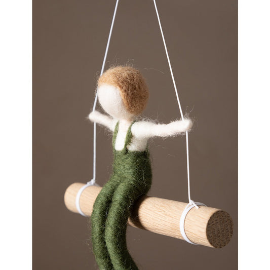Textile figure of a person in green overalls on a swing against a brown background