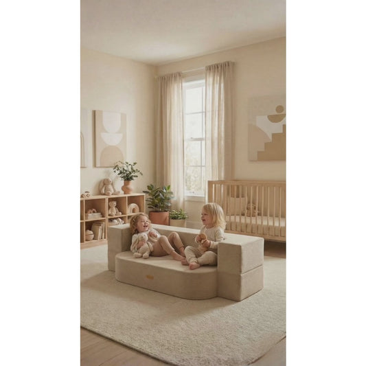 Two children sitting on a beige play couch in a nursery with a crib and decor.