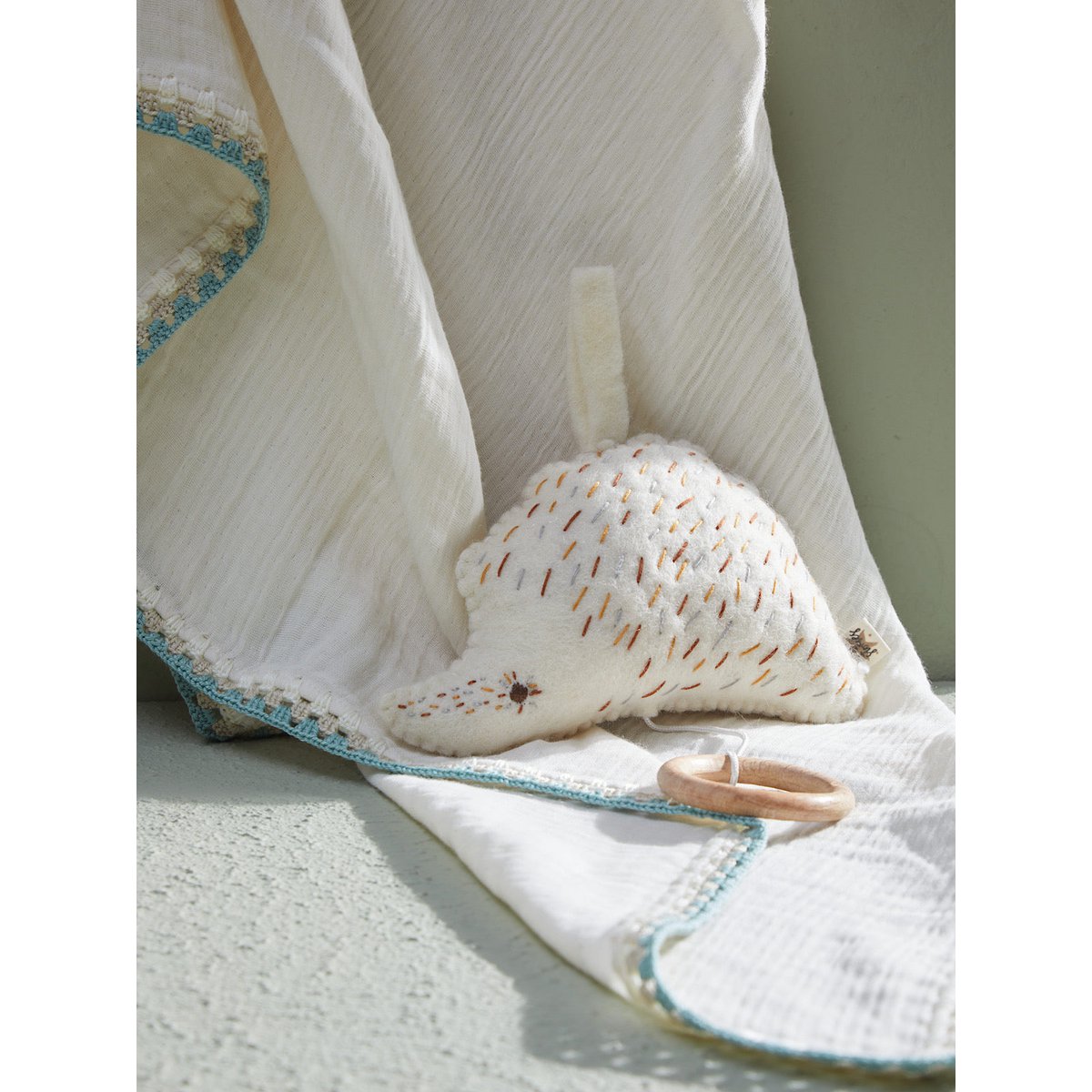 Baby helmet and teething ring on a white blanket with a soft focus background