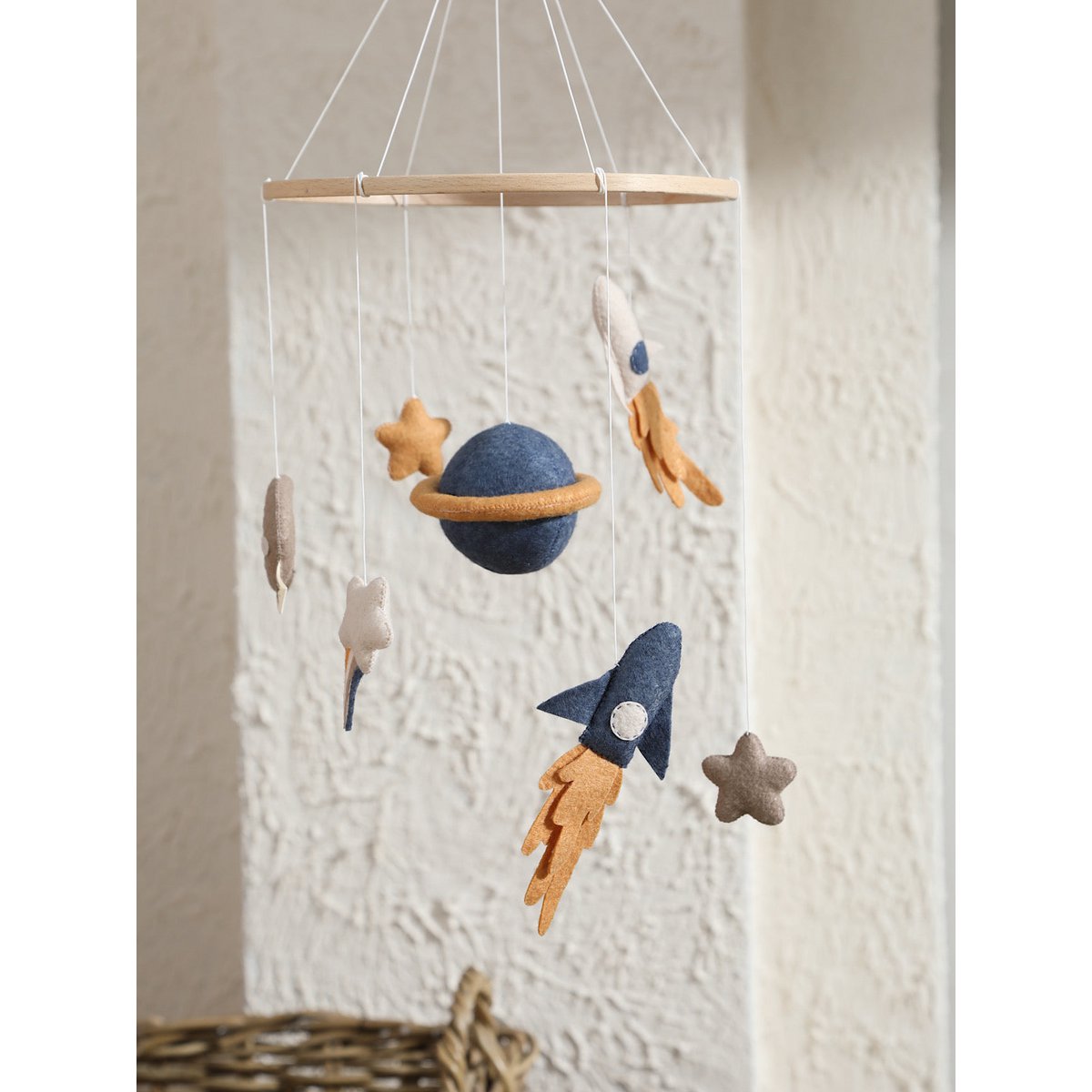 Children's space-themed mobile with planets, rockets, and stars hanging against a textured wall.