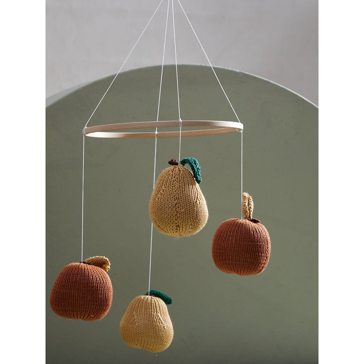 2 stories Knitted fruit mobile with brown and beige apples hanging from strings against a neutral background