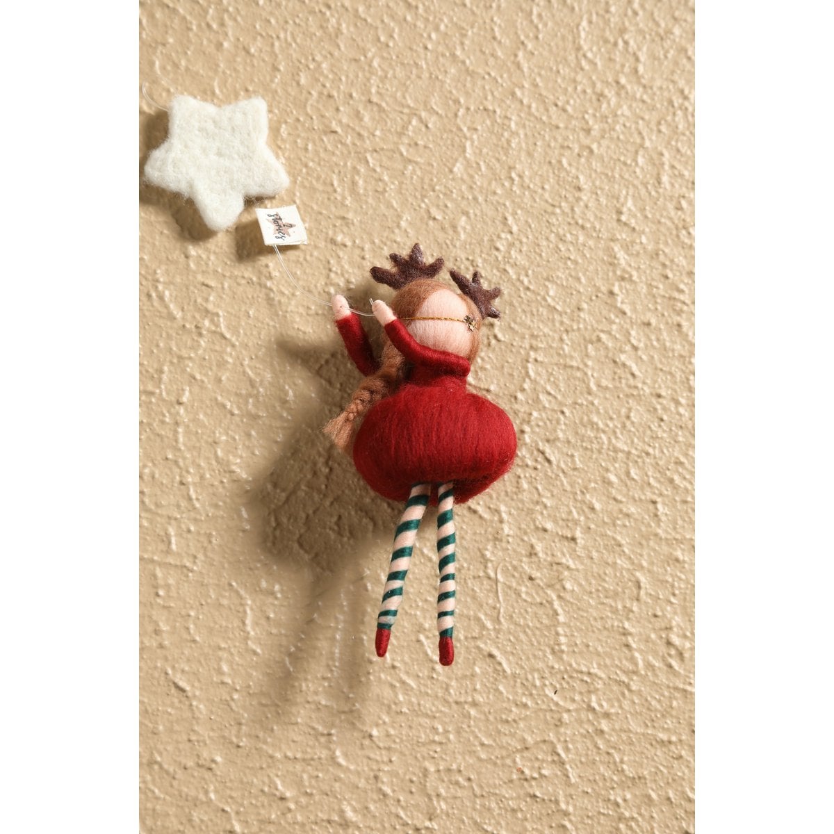 Small stuffed reindeer toy hanging on a textured beige wall with a white star above it.