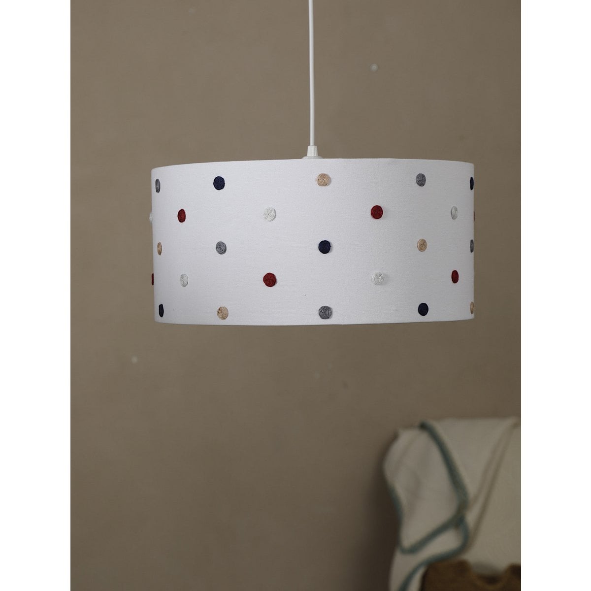 White lampshade with colorful polka dots hanging against a beige wall.