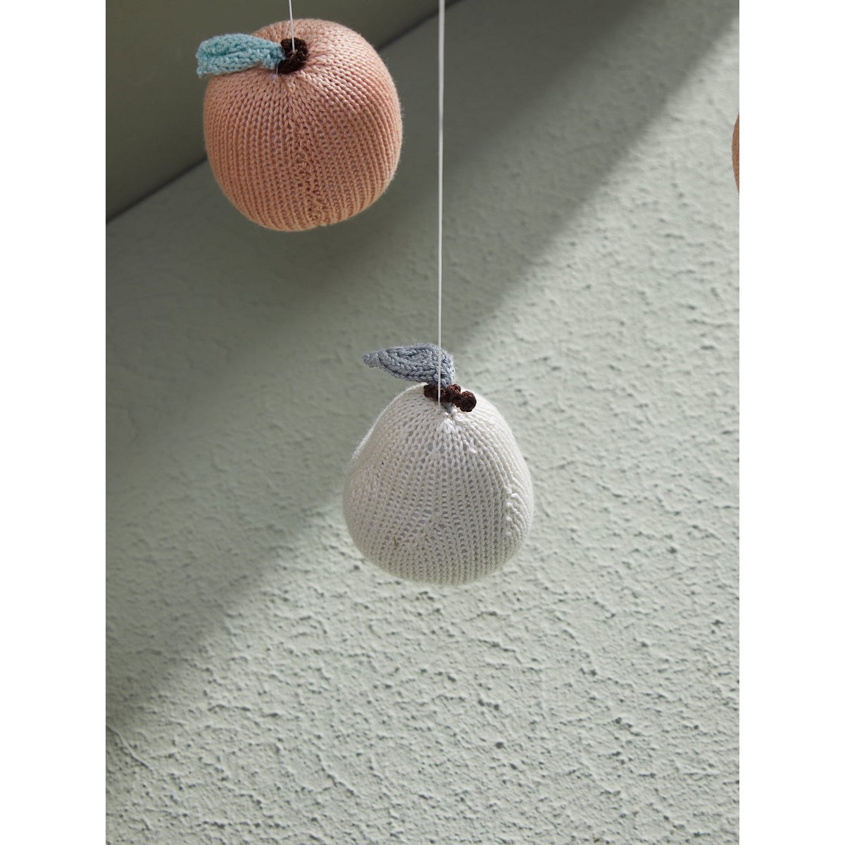 Knitted apple-shaped objects hanging on a textured surface