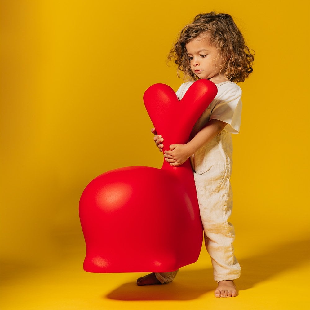 Child holding a red heart-shaped chair against a yellow background