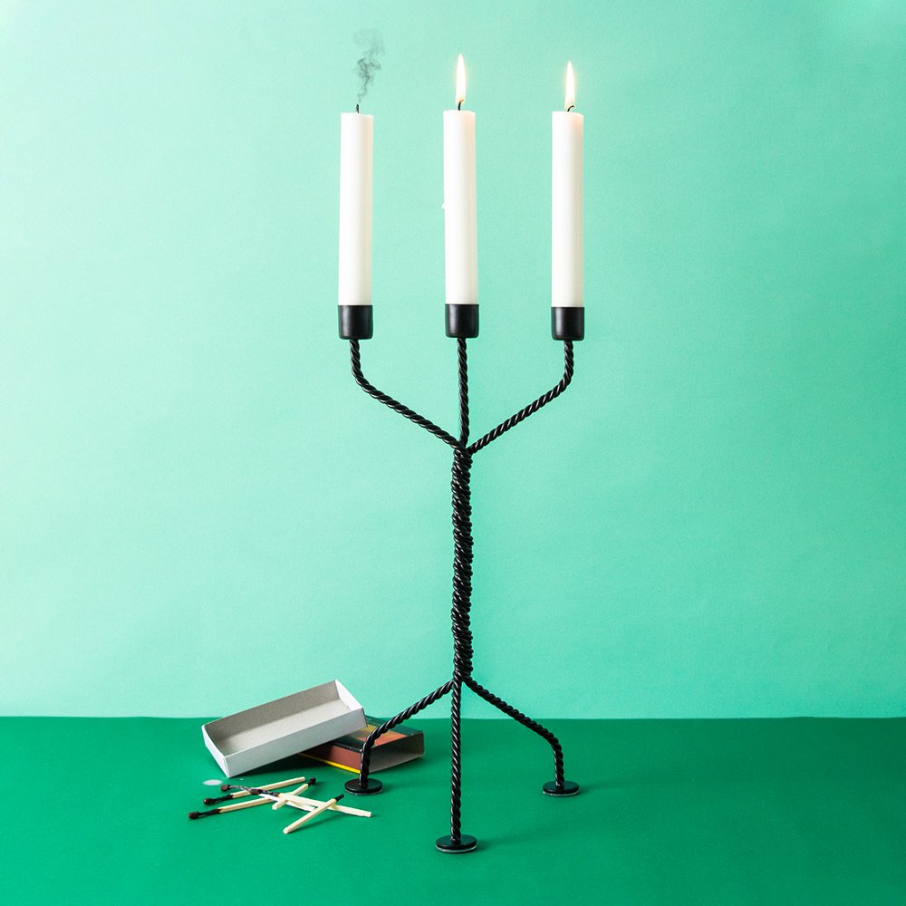 Black candle holder with three white candles on a green background