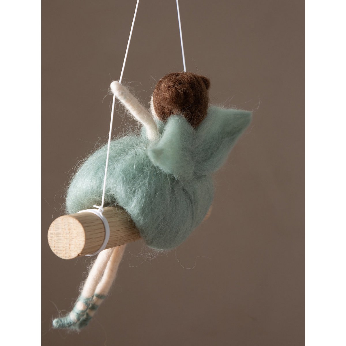 Felted fairy figurine on a swing against a brown background