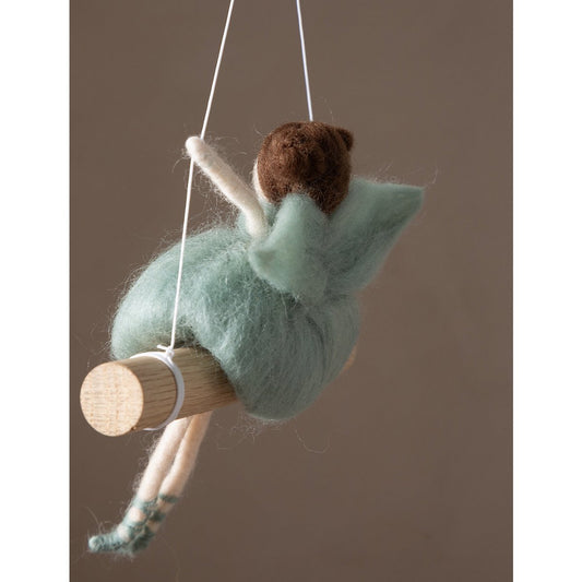 Felted fairy figurine on a swing against a brown background