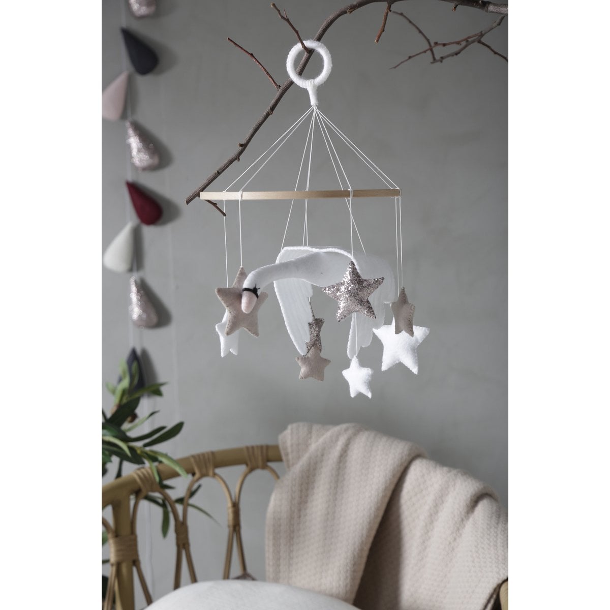 Star-shaped decorative mobile hanging against a neutral wall with a chair and blanket in the foreground.