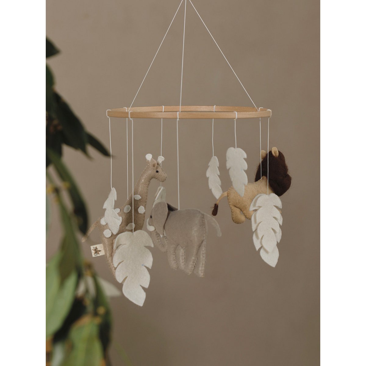 Children's mobile with animals and leaves hanging against a beige wall.