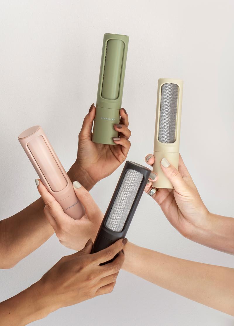 Four hands holding different colored pet hair removal tools against a light gray background
